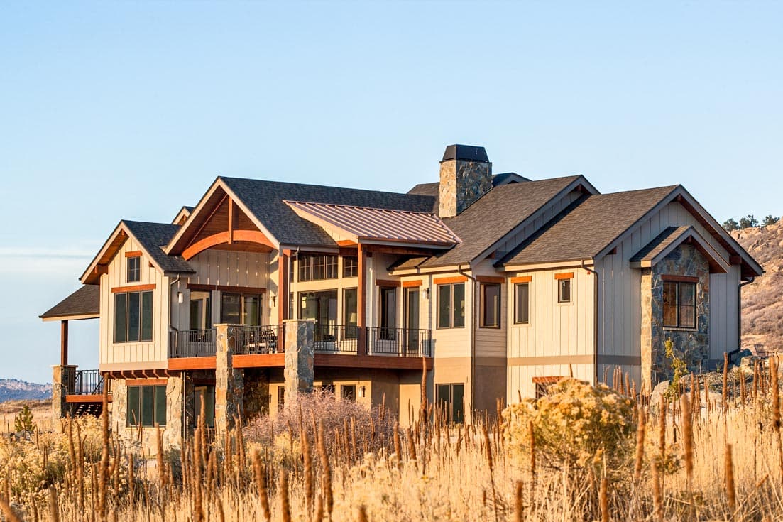 House plan exterior: Lodge style, multi-level home with stone accents, prominent gables, large windows, and a metal roof section.