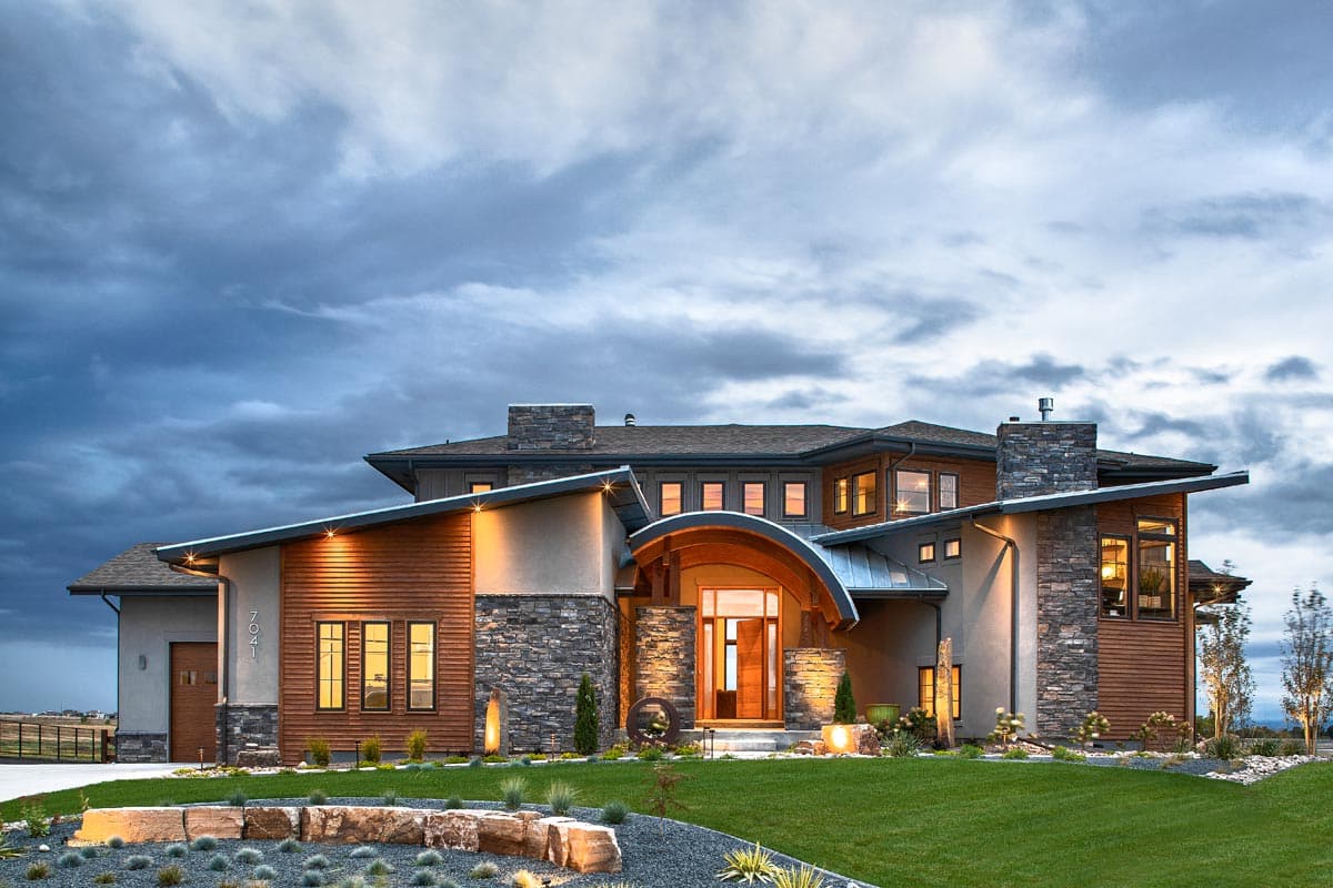 House plan exterior. Modern style, multi-story home with a curved entryway, asymmetrical rooflines, and stone accents. Features a detached garage.