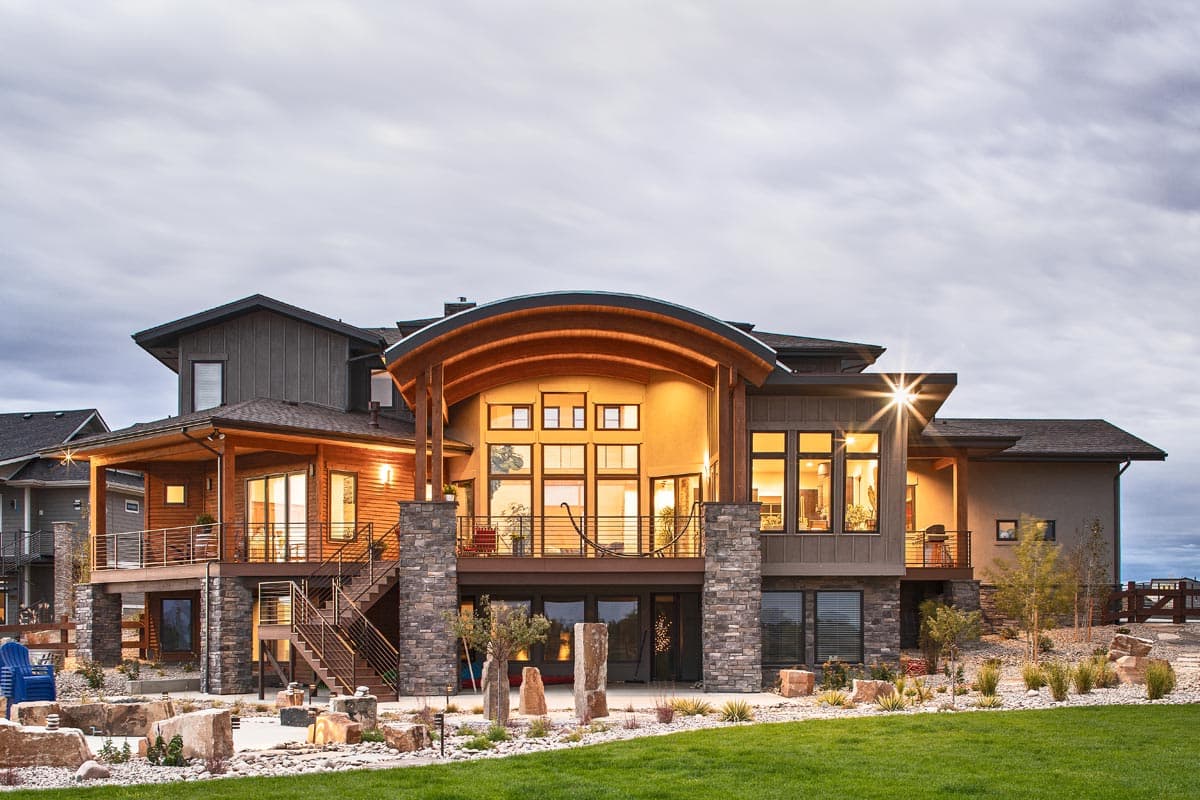 Modern house exterior with wood siding, stone accents, multiple levels, covered deck, and curved roofline.