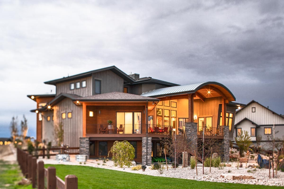 Modern house plan exterior with multiple gables, curved roofline, stone accents, and extensive windows.