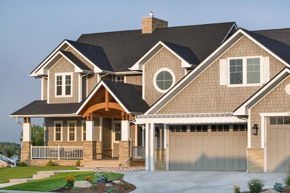 House plan exterior: Two-story home with gabled rooflines, shingle siding, stone accents, covered porch, and attached garage.