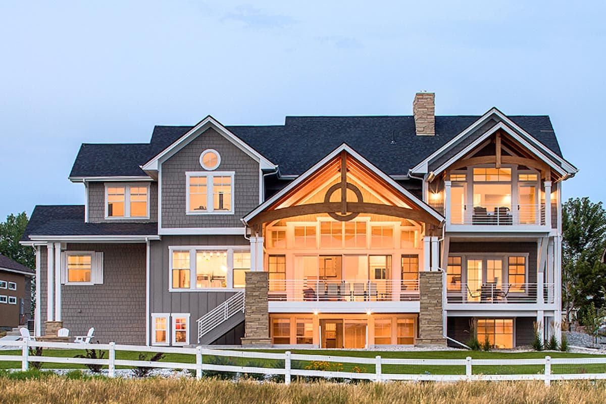 House plan exterior: Three-story home with a prominent gabled entry, large windows, balconies, and a stone chimney.