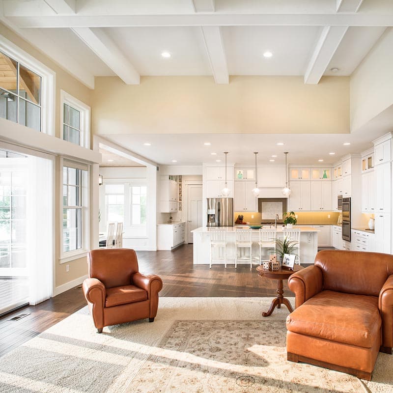 Open concept living space with vaulted ceiling, exposed beams, large windows, and white kitchen island.