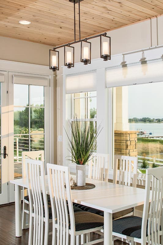 Interior dining room with a white table and chairs, large windows, and a contemporary pendant light fixture.