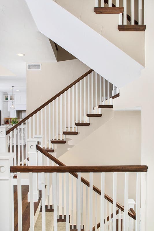 Interior view of a two-story staircase with white balusters, dark wood handrails, and treads.