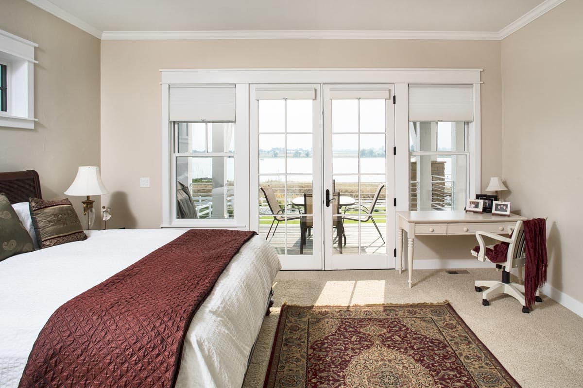 Bedroom with bed, desk, and french doors opening to a deck with water view.