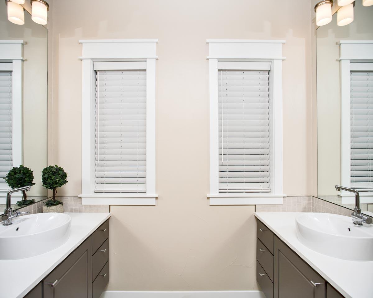 Double vanity bathroom with two vessel sinks, dark gray cabinetry, white quartz countertops, and dual windows with blinds.