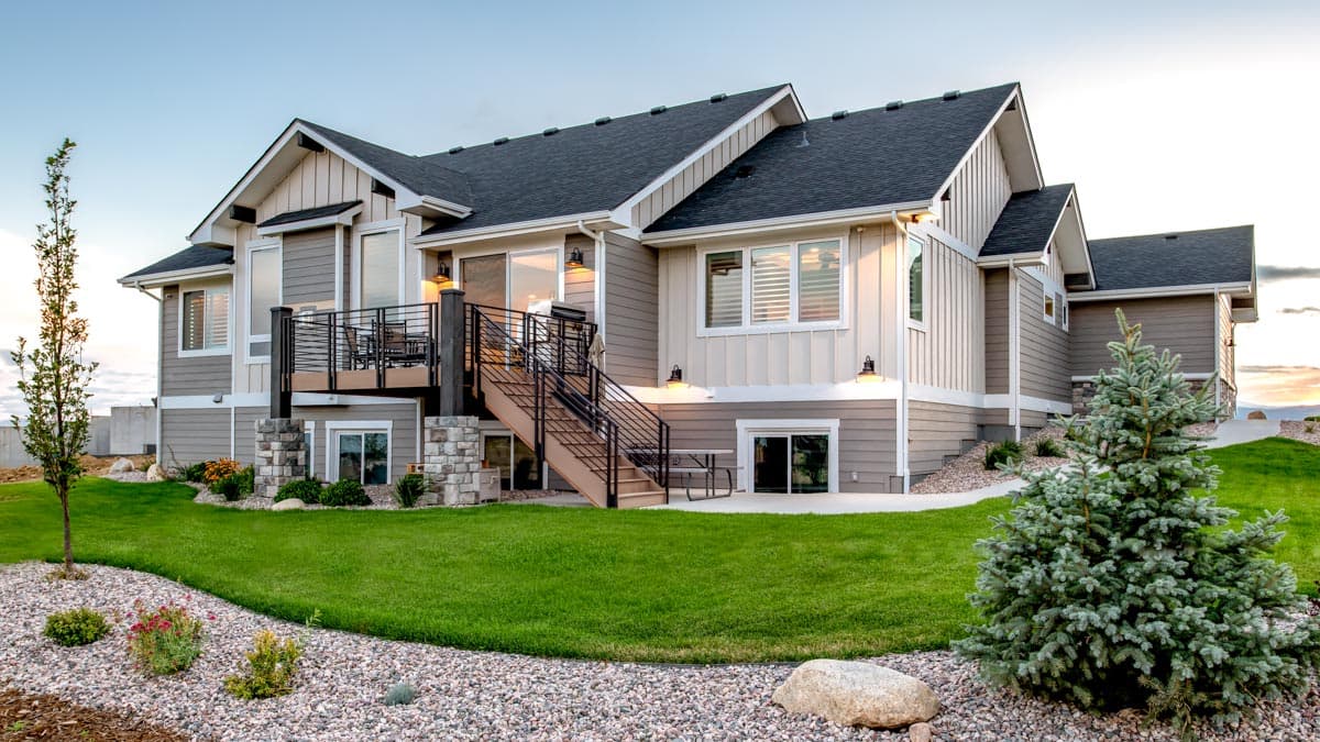 Modern house exterior with multi-level rooflines, large windows, deck with stairs, and stone-clad supports.