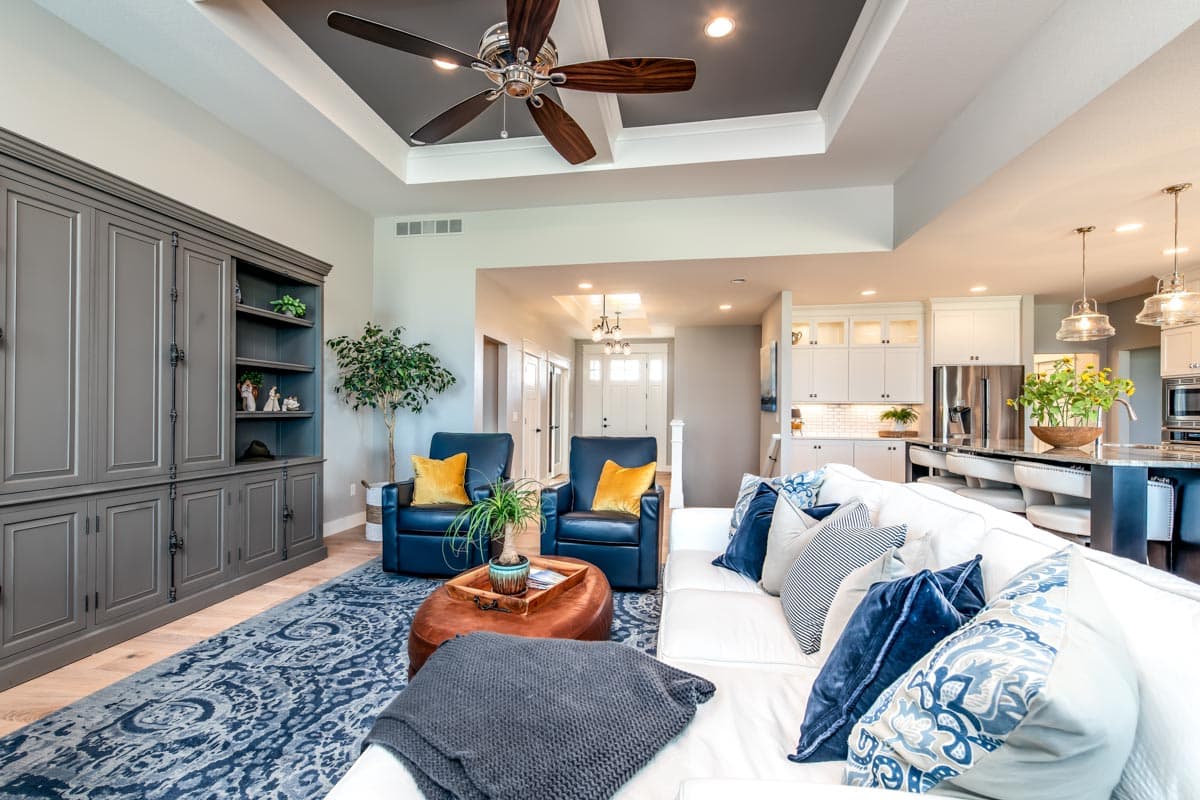 Interior view of living room with built-in cabinets, two armchairs, and open access to kitchen with island and white cabinetry.