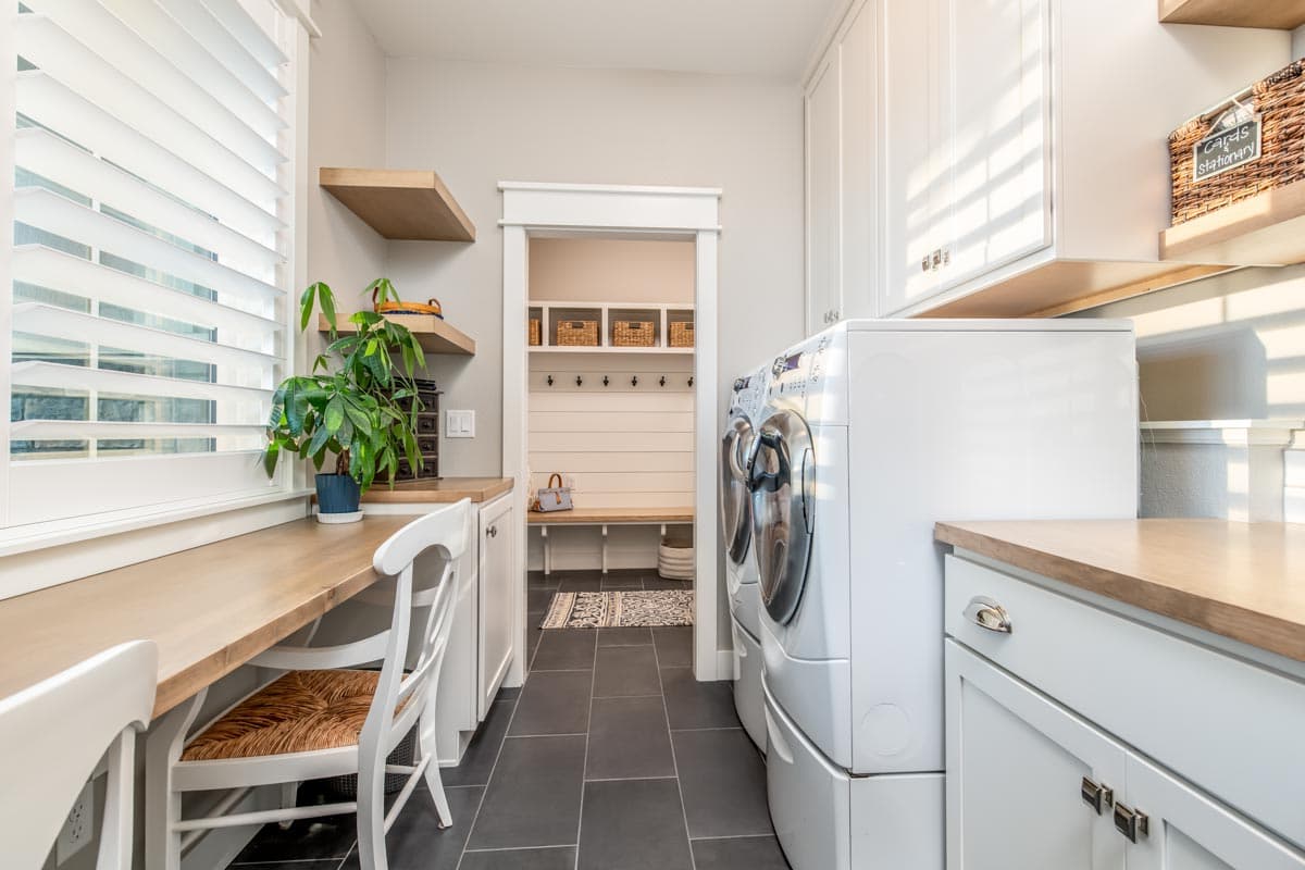 Laundry room with white cabinets, wood countertops, washer and dryer, built-in bench and cubbies visible through doorway.