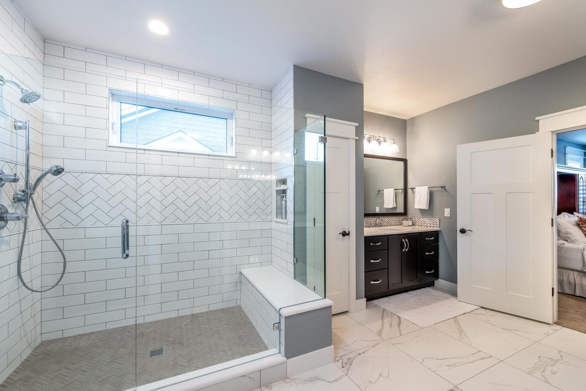 Modern bathroom with glass-enclosed shower featuring subway tile and herringbone floor, double vanity with dark cabinetry, and marble tile flooring.