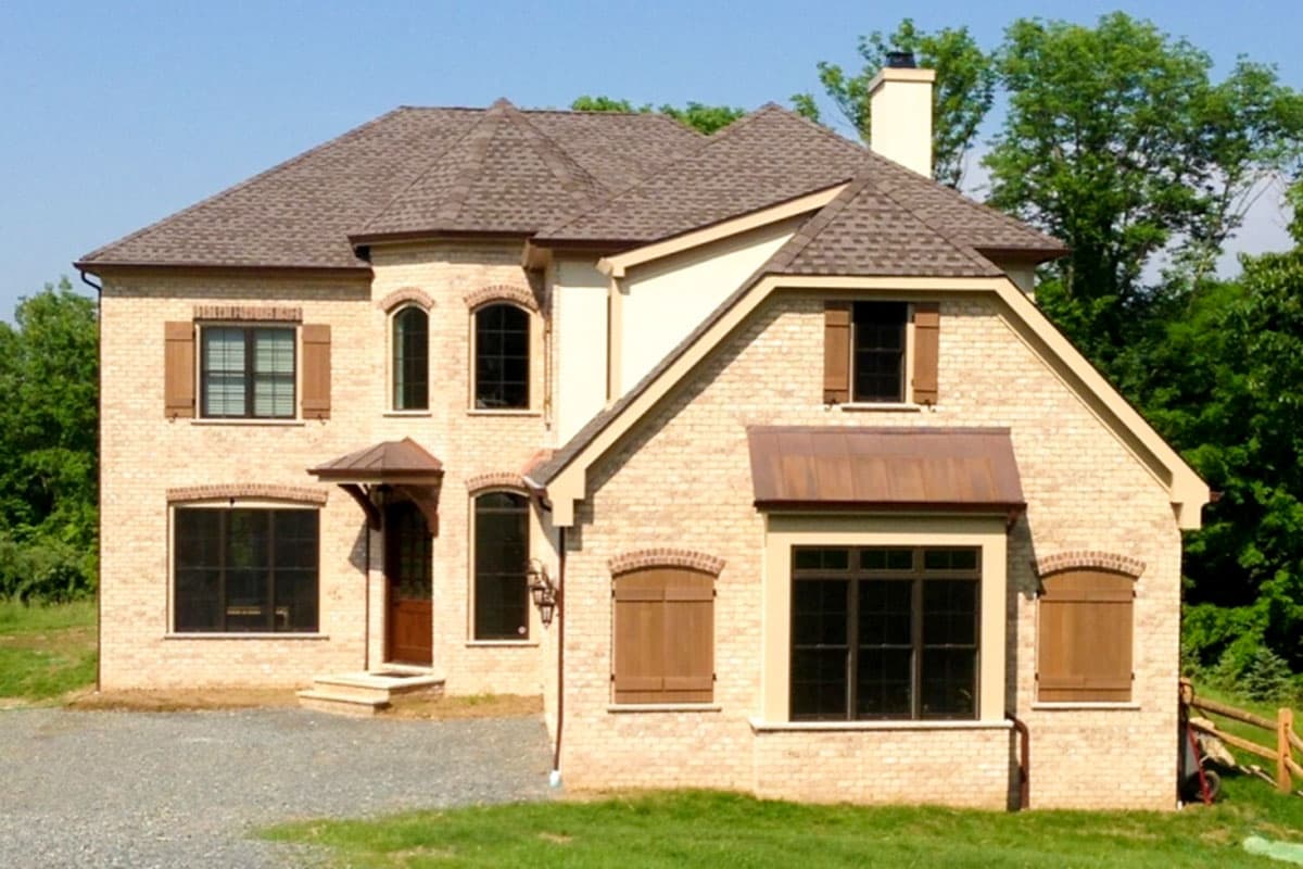 Two-story brick house plan exterior with arched windows, shutters, a prominent roofline, and copper awnings.