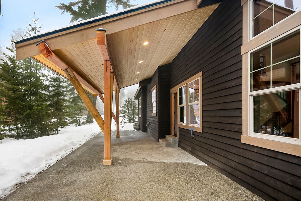 House plan exterior with dark wood siding, wood-framed porch with exposed beams and vaulted ceiling.