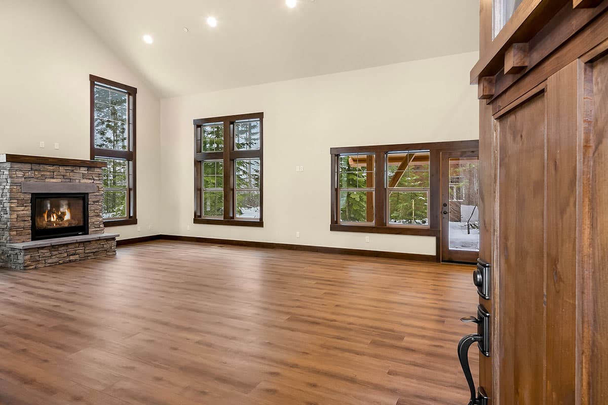 Interior view of a great room with a stone fireplace, vaulted ceiling, and large windows overlooking trees.