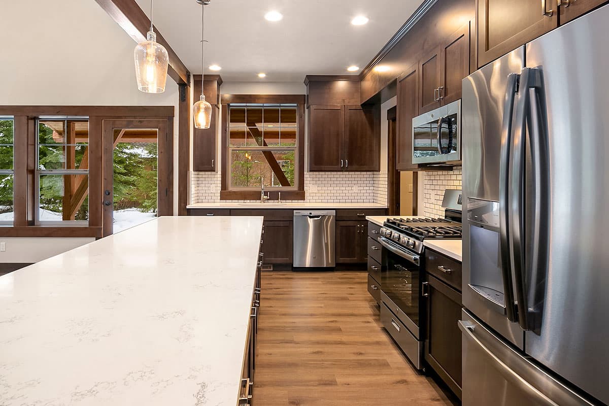 Kitchen with dark wood cabinets, white subway tile backsplash, large island, stainless steel appliances, and exposed wood beams.