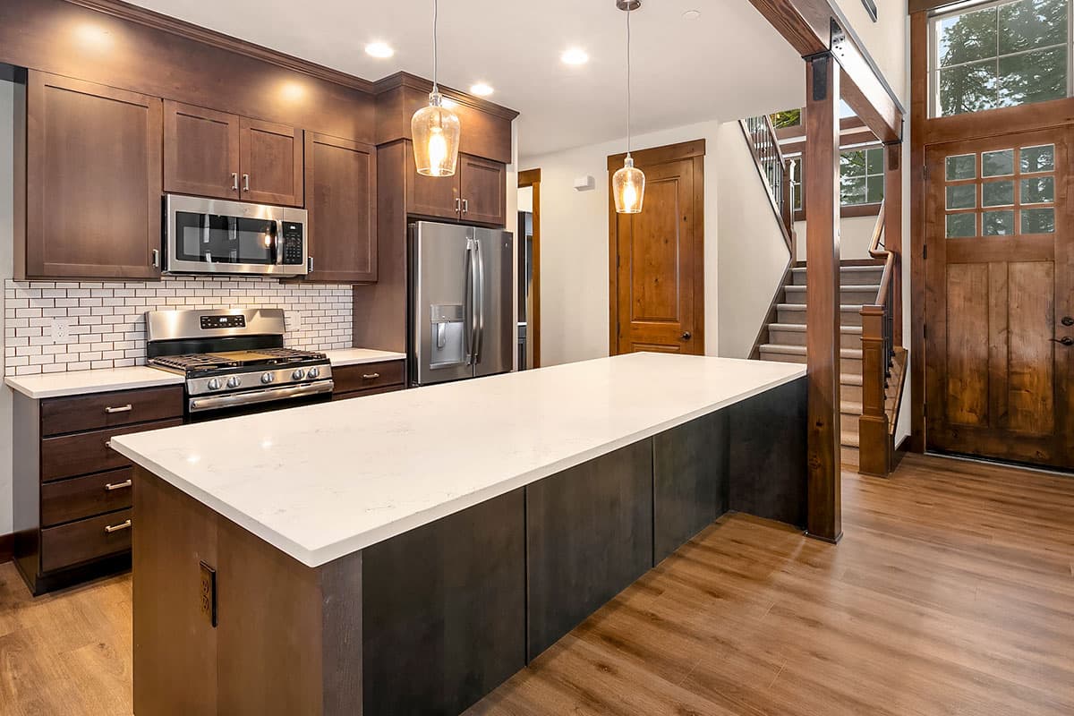 Kitchen with large island, subway tile backsplash, stainless steel appliances, and wood accents. Stairs and entry door visible.