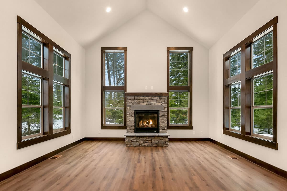 Interior view of great room with stone fireplace, vaulted ceiling, and large wood-framed windows.
