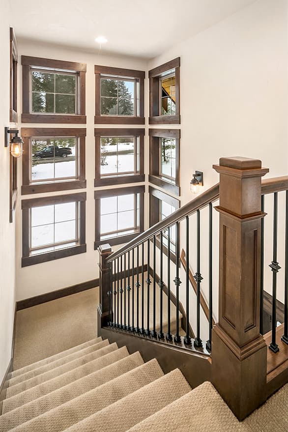 Interior view of a staircase with wood trim windows showing a snowy landscape and a dark wood banister with black spindles.