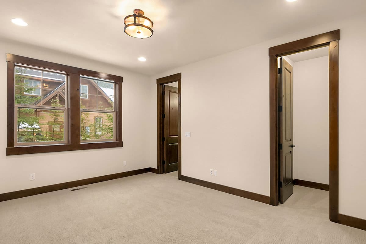 Interior view of a room with carpet, wood trim, a flush-mount light fixture, and two doorways leading to other rooms.