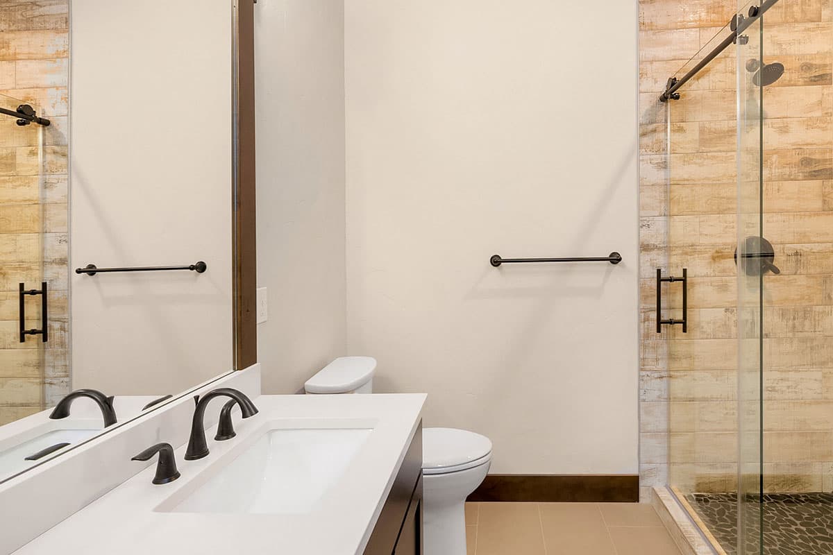 Bathroom with vanity, toilet, and glass-enclosed shower with wood-look tile.