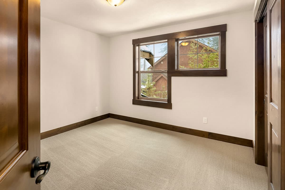 Interior view of bedroom with textured carpet, dark wood trim, double pane windows, and paneled door.