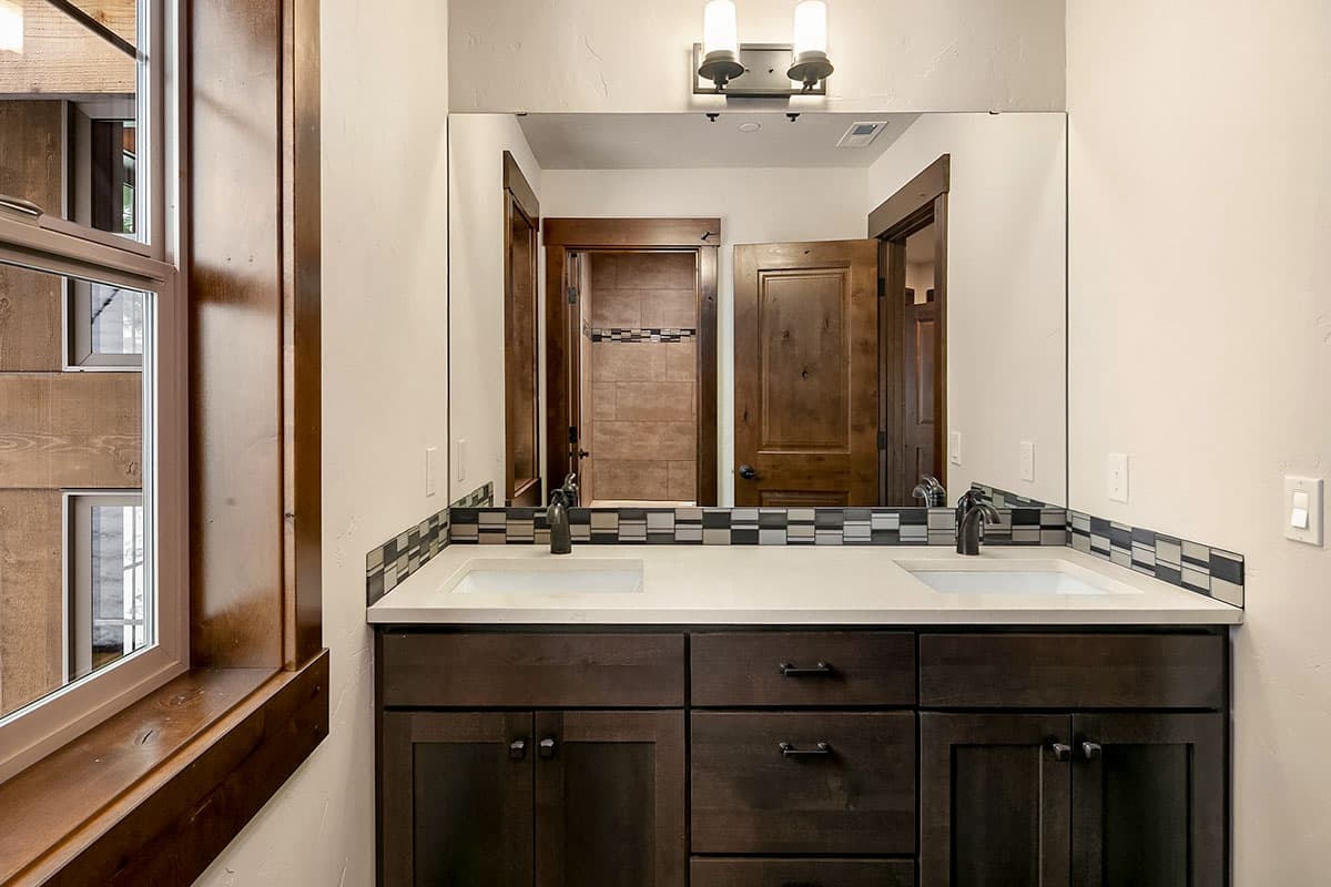 Bathroom vanity with double sinks, dark wood cabinets, mosaic tile backsplash, and twin sconce lighting.