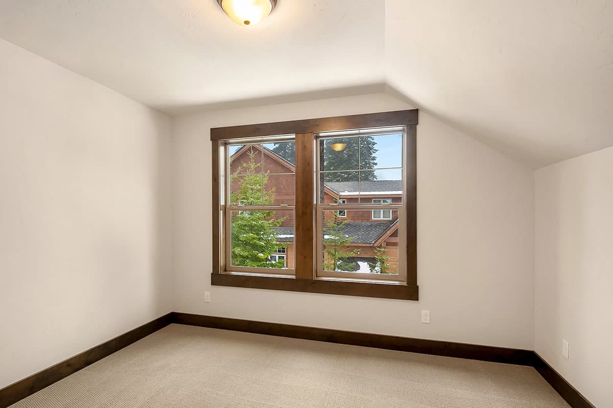 Interior view of a room with a double-hung window with wood trim, looking out at a neighboring house.