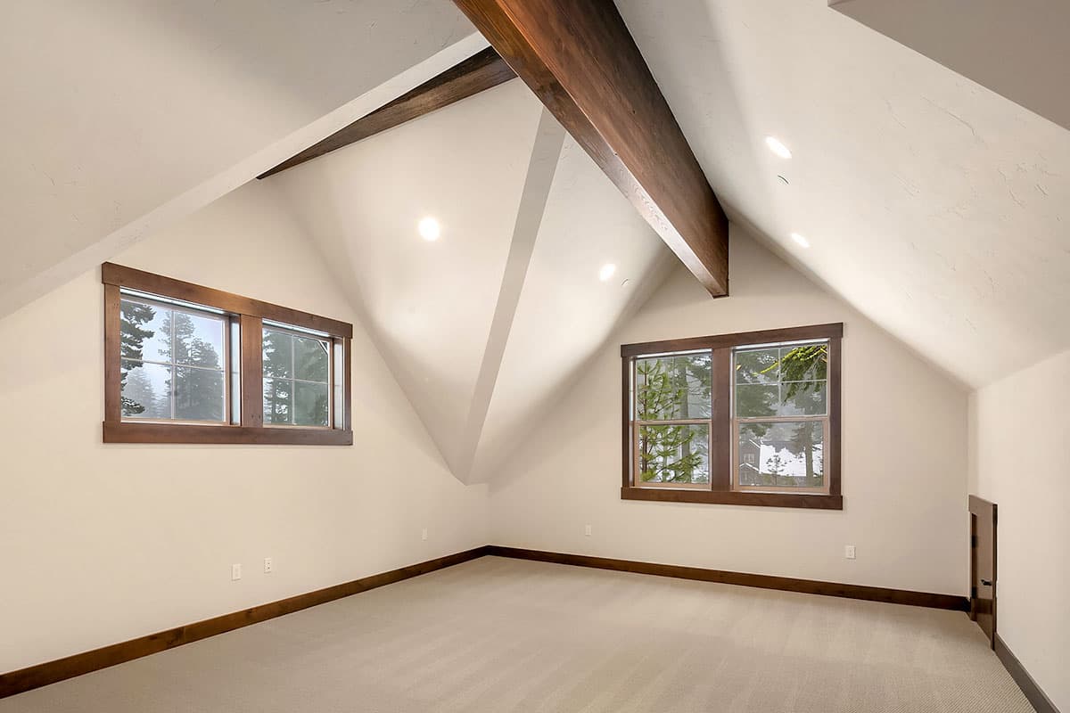 Interior view of a room with vaulted ceilings, exposed wood beams, and two large windows.