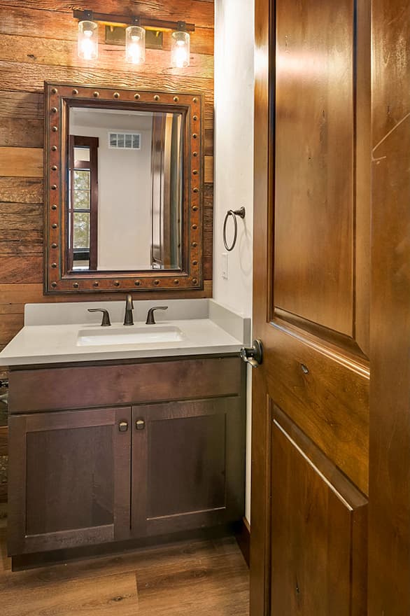 Powder room vanity with dark wood cabinets, quartz countertop, metal-frame mirror, and rustic wood accent wall.