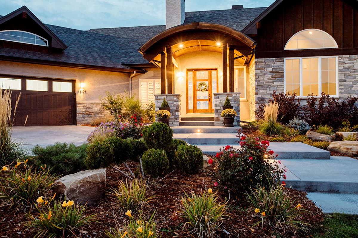 Exterior view of a two-story house with a two-car garage, stone and stucco facade, arched entry porch, and multiple gables.