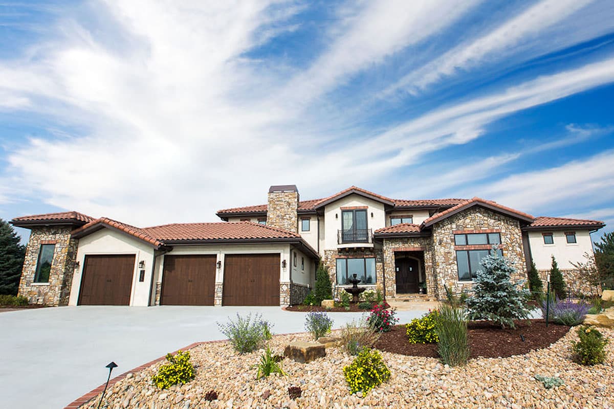 House plan exterior: Large Mediterranean-style residence with stucco, stone accents, tile roof, and three-car garage.