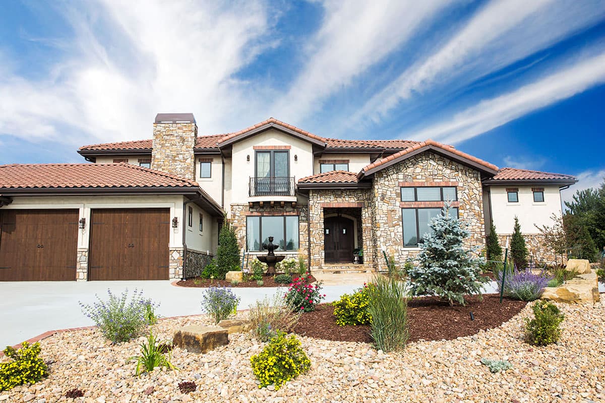 Two-story house plan exterior with stone facade, clay tile roof, attached two-car garage, and arched entryway.