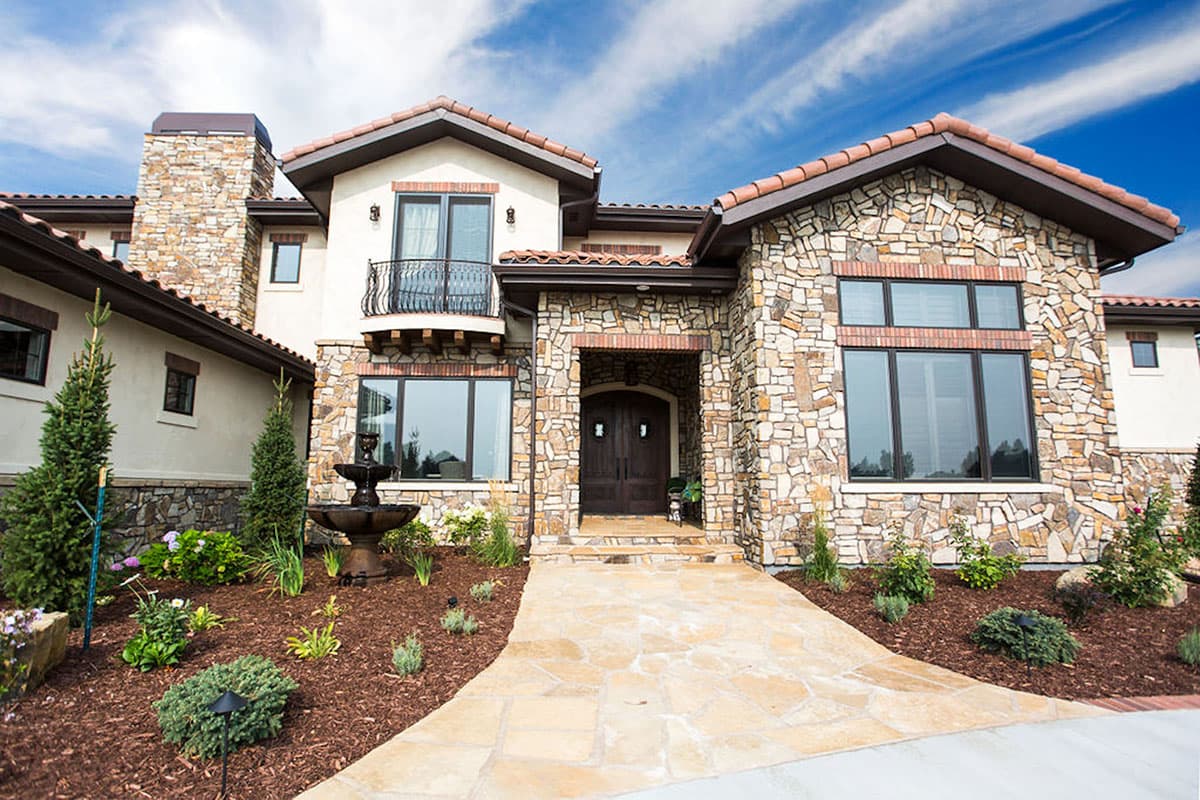 House plan exterior with stone facade, arched entryway, double doors, wrought iron balcony, and tile roof.