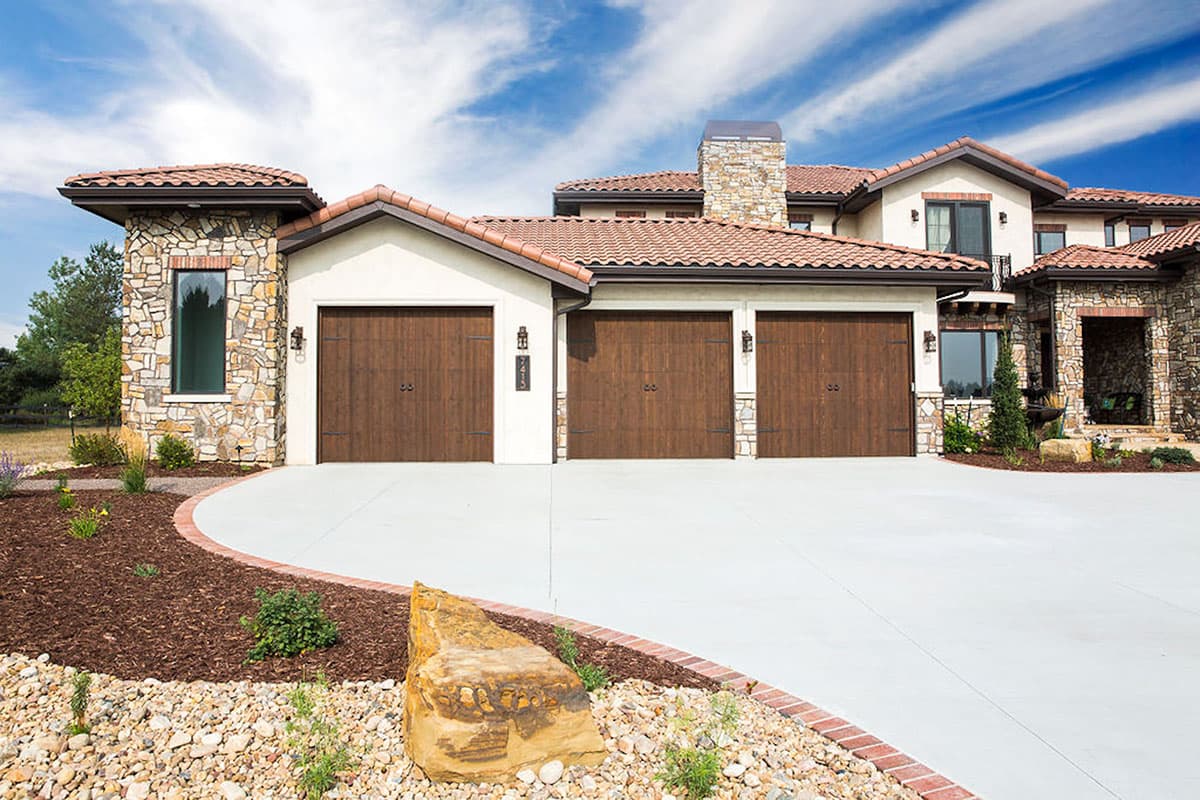 House plan exterior showcasing a Spanish Mediterranean style with a three-car garage, tiled roof, and stone accents.