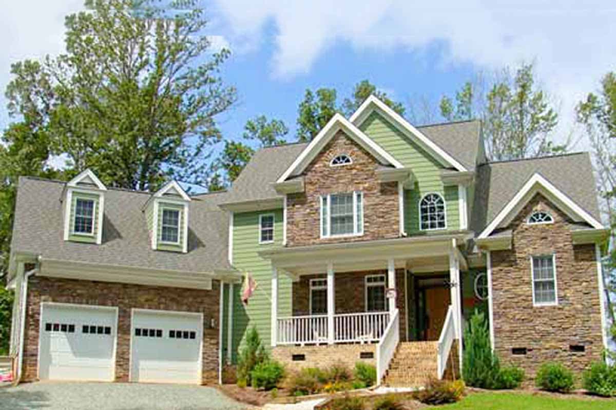 House plan exterior: two-story, mixed stone and green siding, front-facing gable with dormers, covered front porch, side-entry garage.