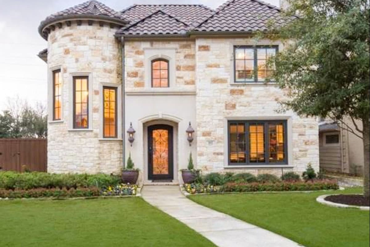 House plan exterior: Two-story residence with a turreting entrance, stone facade, arched entryway, and multi-pane windows.
