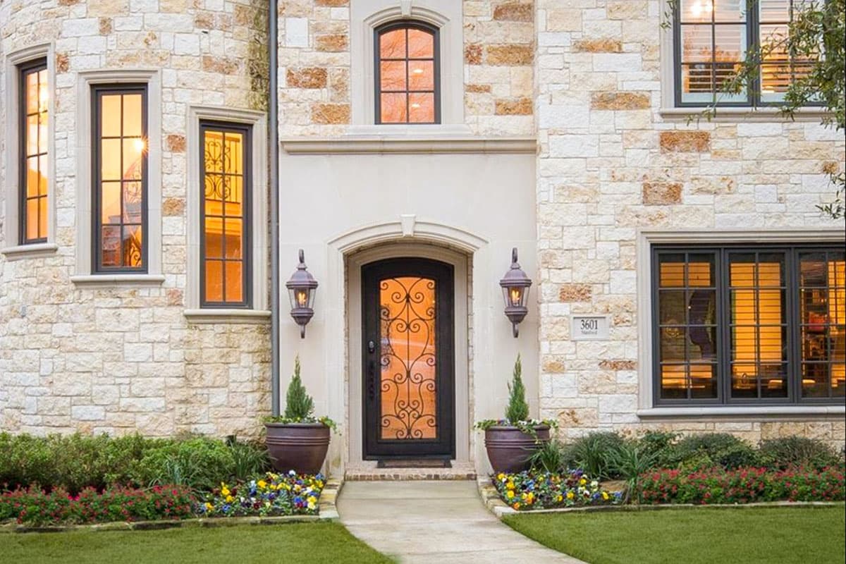 House plan exterior with stone facade, arched entryway with wrought iron door, decorative lanterns, and multi-pane windows.
