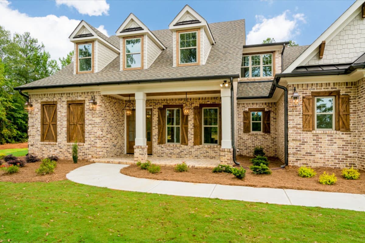 House plan exterior: Brick two-story with gabled dormers, covered porch with white columns, and wooden shutters.