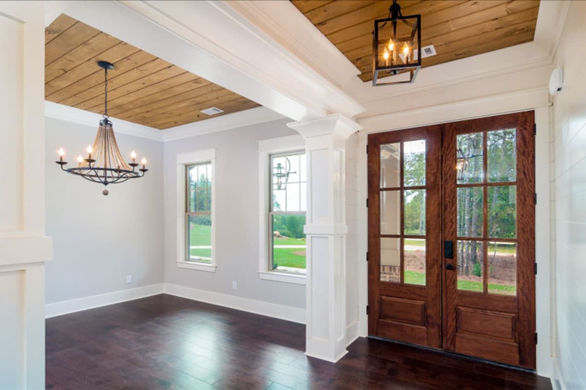 Interior view of entryway with double wooden doors, coffered wood ceilings, and two windows.