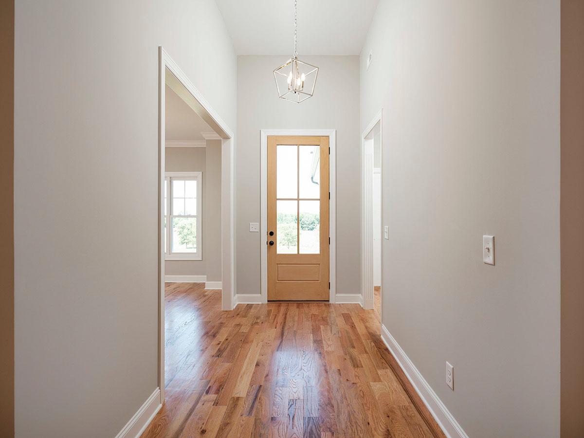 Interior view of a house entryway with a glass-paneled wooden door, hardwood floors, and a modern pendant light.