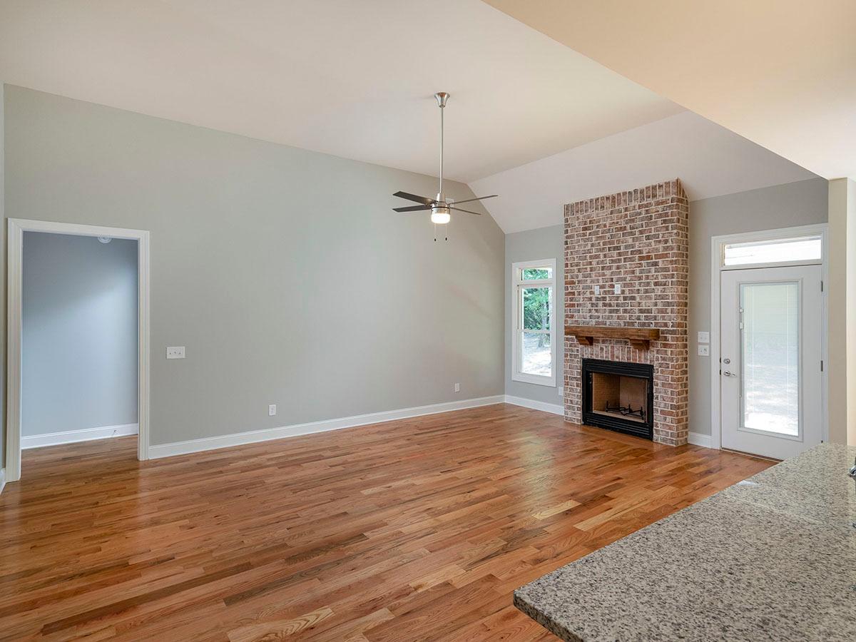 Great room with vaulted ceiling, brick fireplace, hardwood floors, ceiling fan, and interior door.