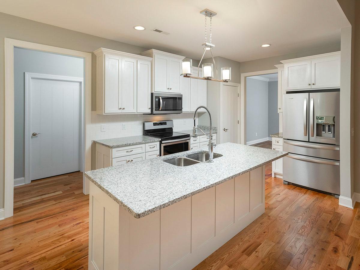Kitchen with white shaker cabinets, granite countertops, central island with sink, and stainless steel appliances.