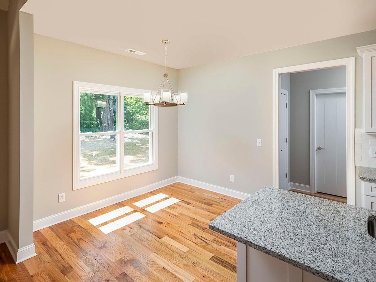 Dining area with large window and chandelier, adjacent to kitchen with granite island. Wooden floors visible.