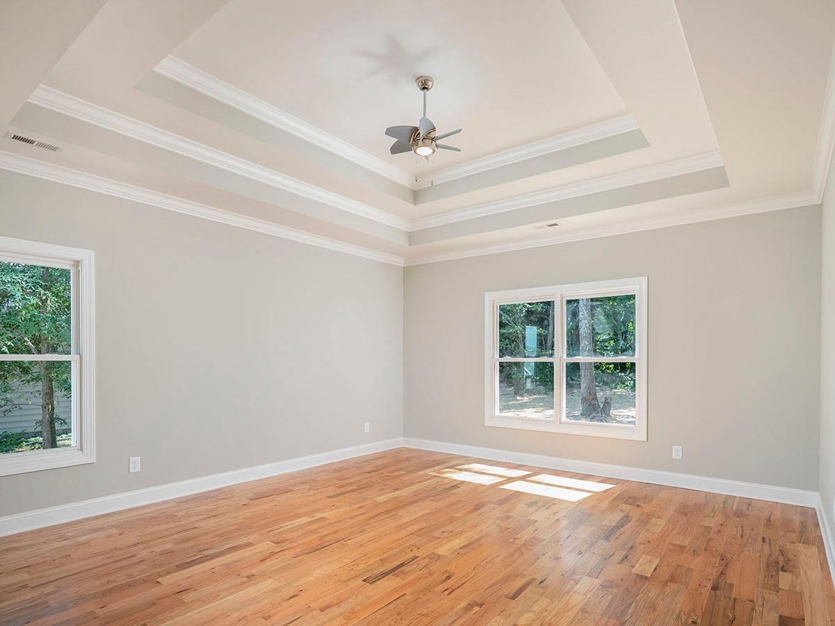 Interior view of an empty room with hardwood floors, large windows, and a coffered ceiling with a fan.