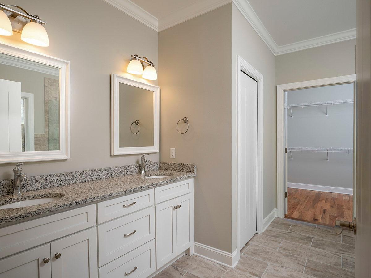 Bathroom vanity with double sinks, granite countertops, mirrors, and access to a walk-in closet with shelving.