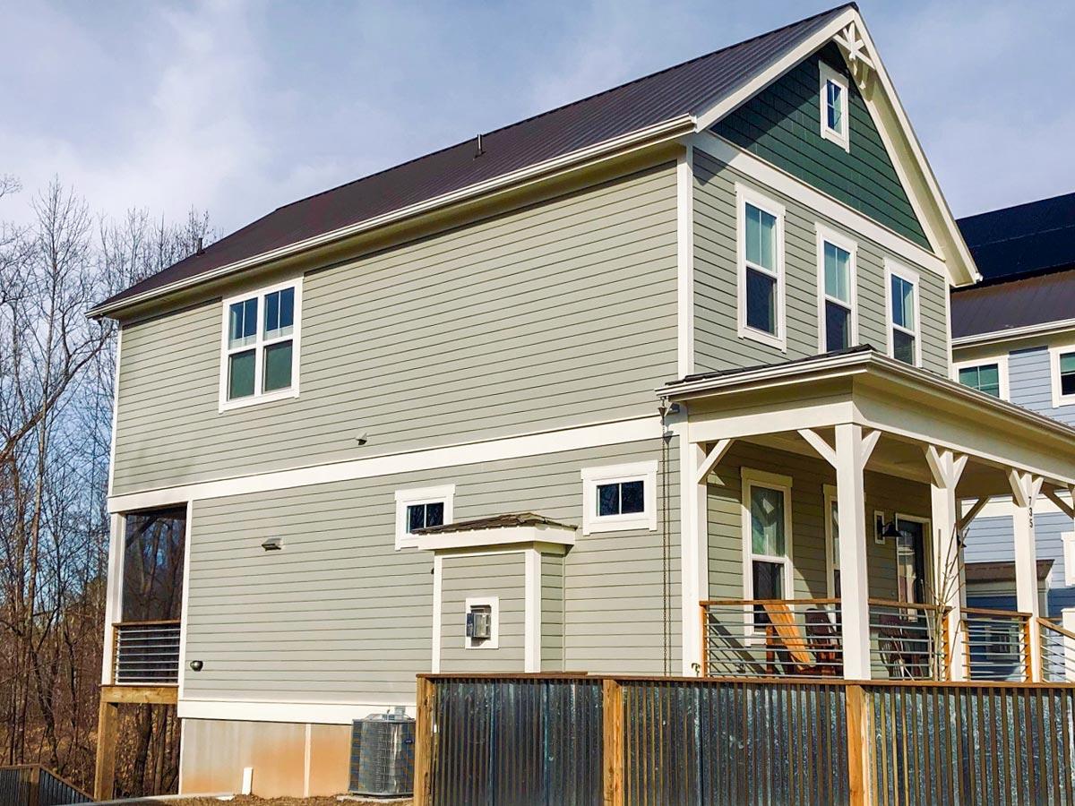 House plan exterior: two-story home with gabled dormer, wide porch, horizontal siding, and metal roof.