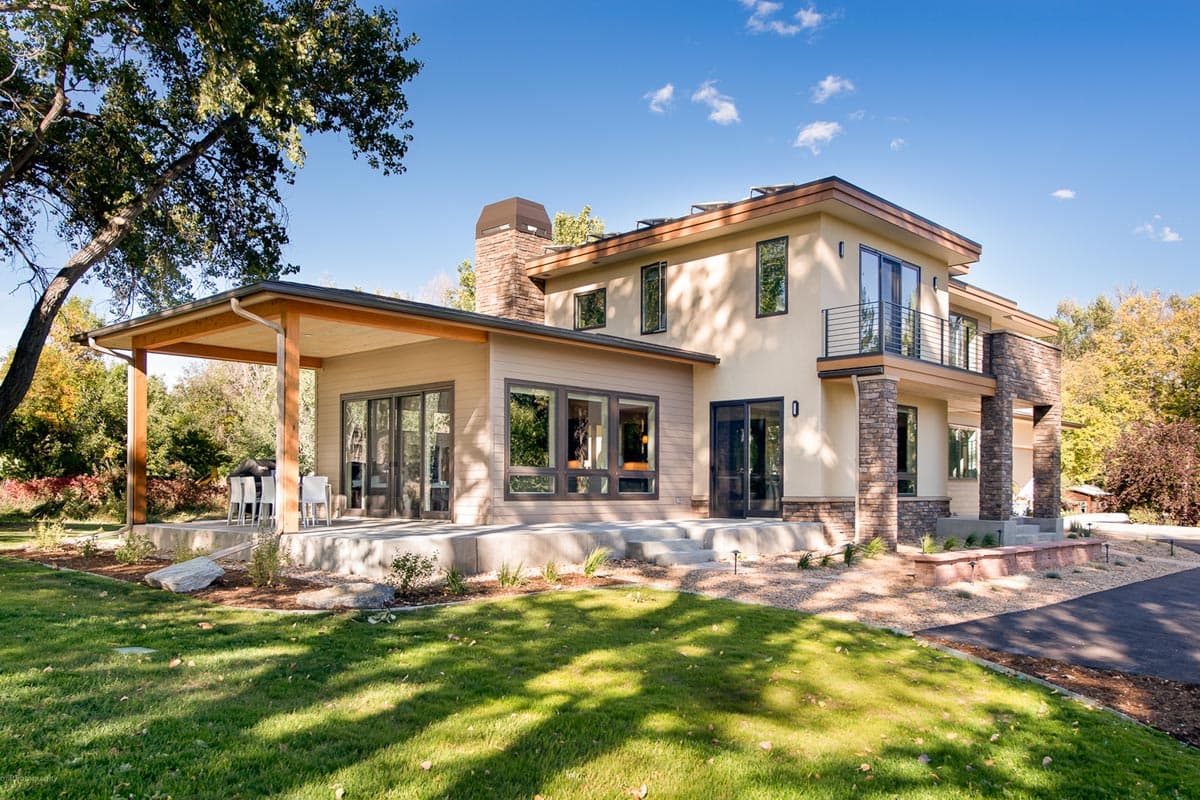 Modern two-story house plan exterior with cantilevered roof, stone accents, large windows, and covered patio.