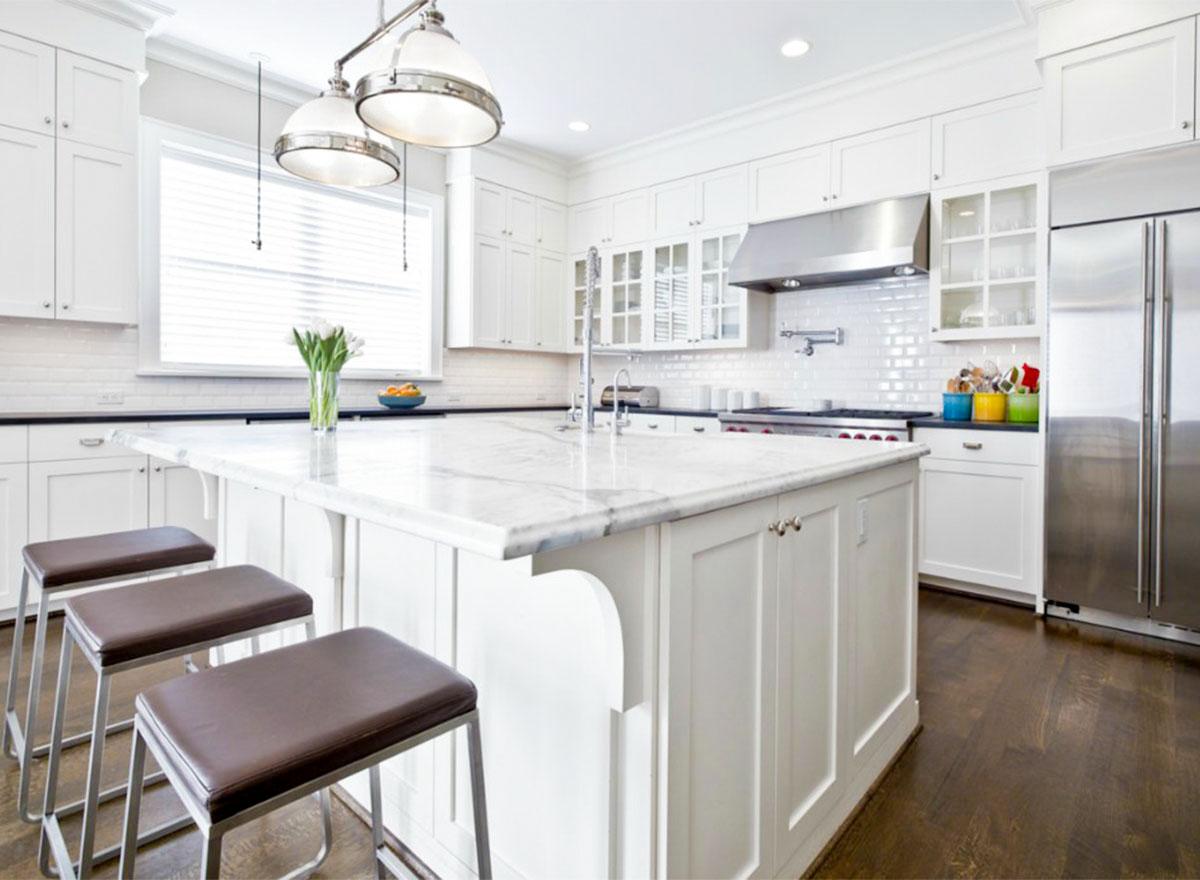 Kitchen with white cabinetry, marble island with seating, stainless steel appliances, and subway tile backsplash.