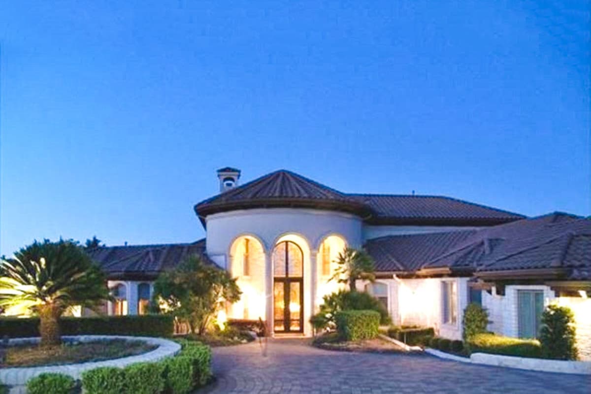 House plan exterior with a curved stucco facade, arched entryway, tiled roof, and multiple gables.