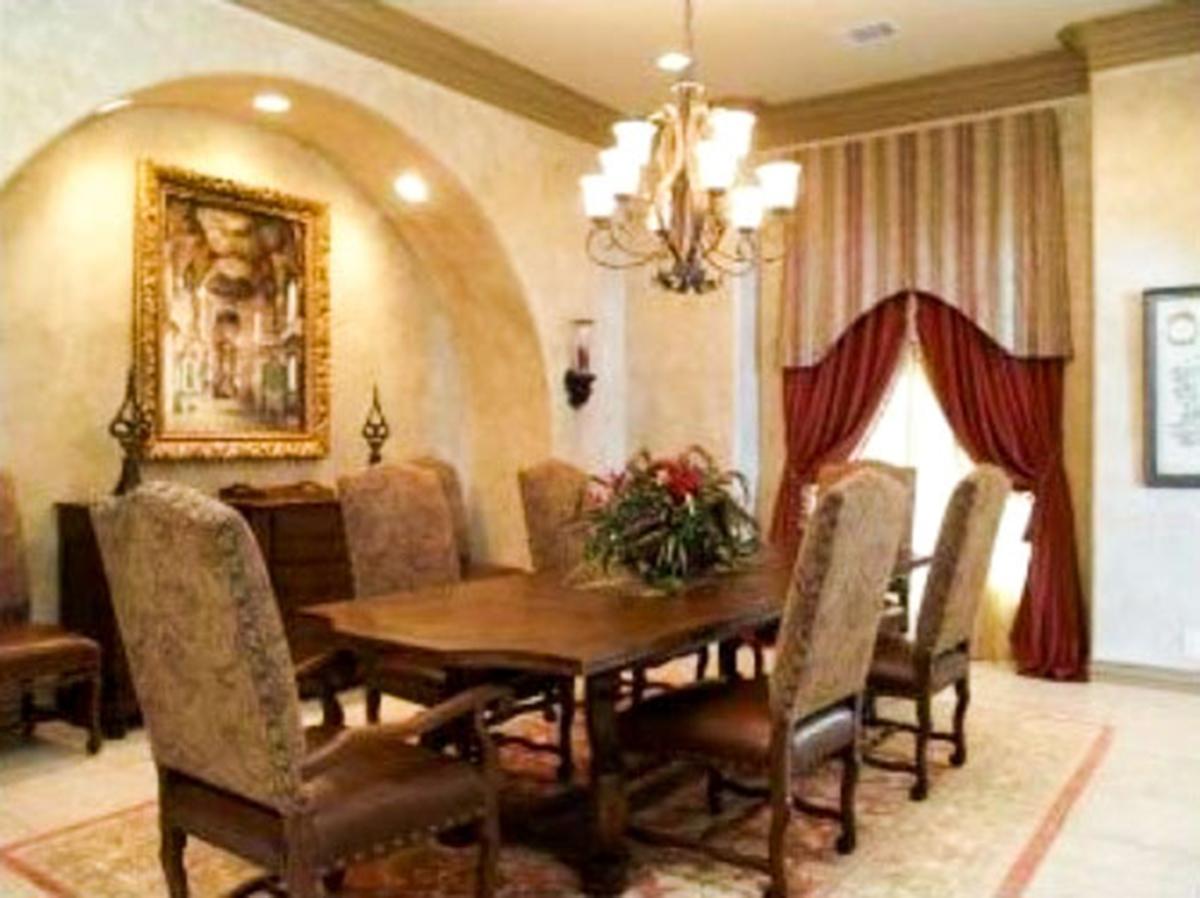 Dining room with ornate chandelier, arched alcove, dark wood table, upholstered chairs, and dramatic drapes.